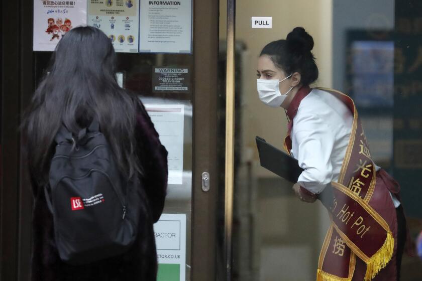 Una empleada de un restaurante de comida china con mascarilla recibe a una clienta en Londres el 5 de marzo del 2020. (AP Photo/Frank Augstein)
