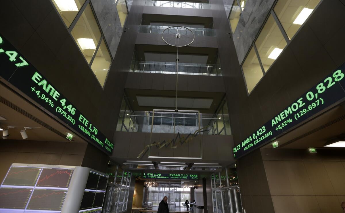 An employee walks under screens showing rising stocks in green in Athens on Tuesday. Greece's creditors in the 19-country eurozone approved Tuesday a list of reforms Athens proposed to get a 4-month extension to its bailout, which should keep the country afloat over the coming months.