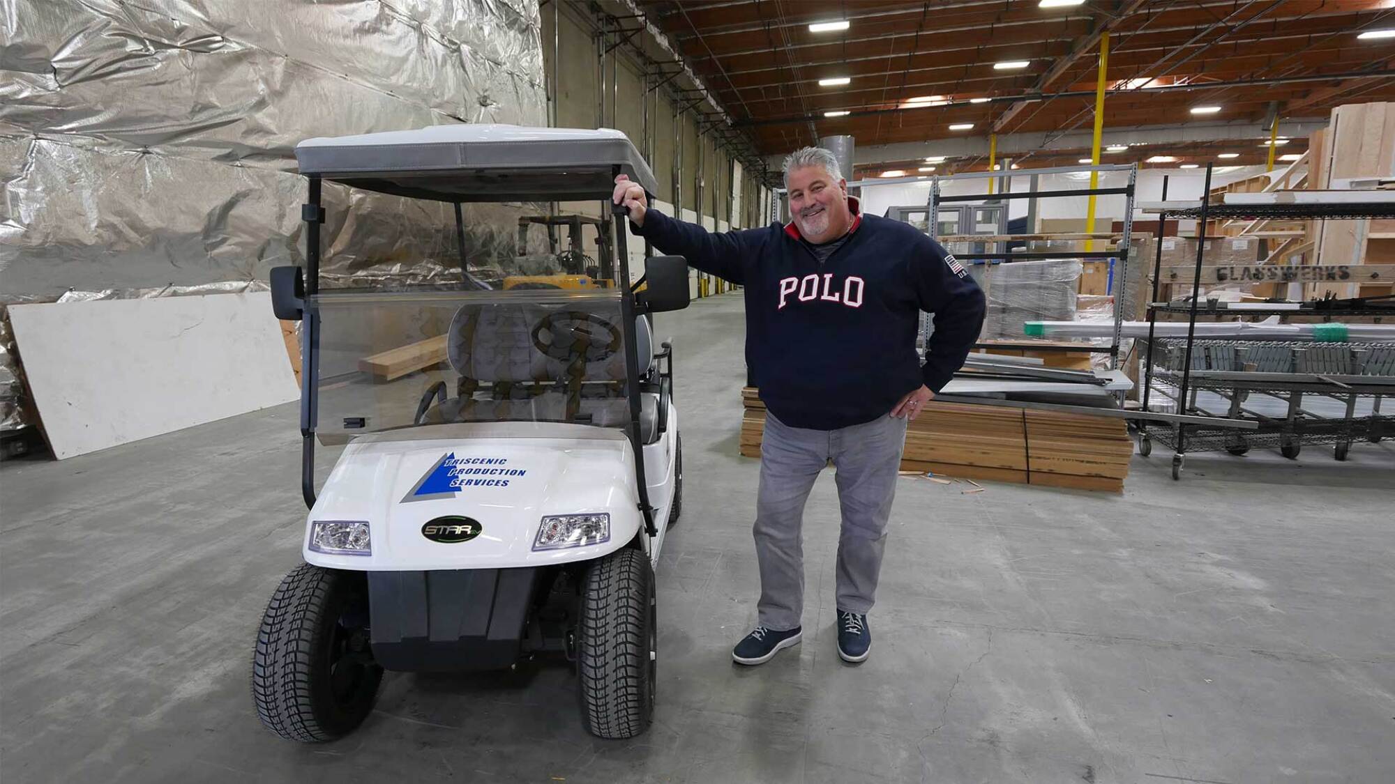 A man in a sweatshirt smiling and posing next to a golf cart on a soundstage