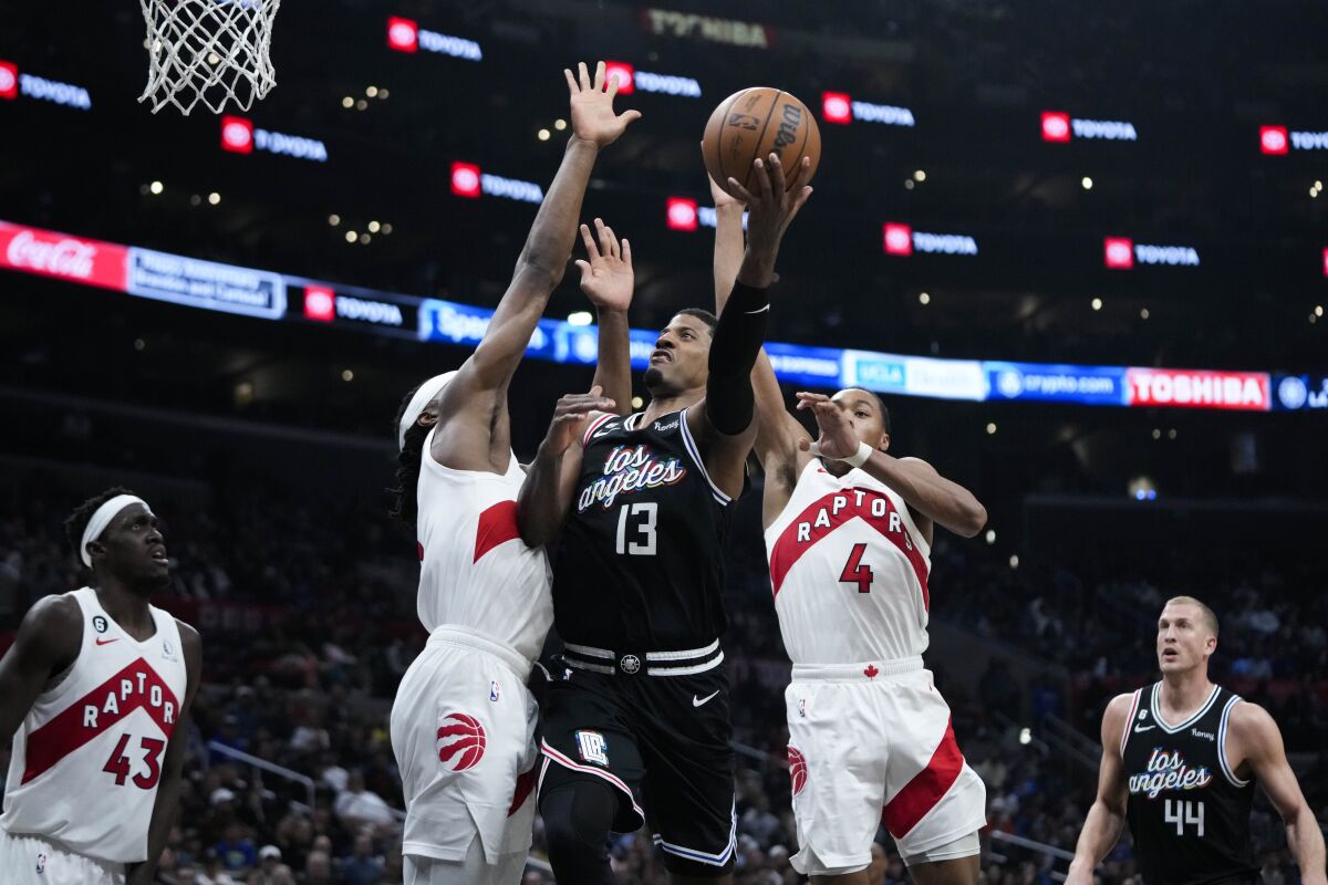 Paul George of the Clippers hits the basket under the protection of Scotty Barnes and Will Burton of the Toronto Raptors.