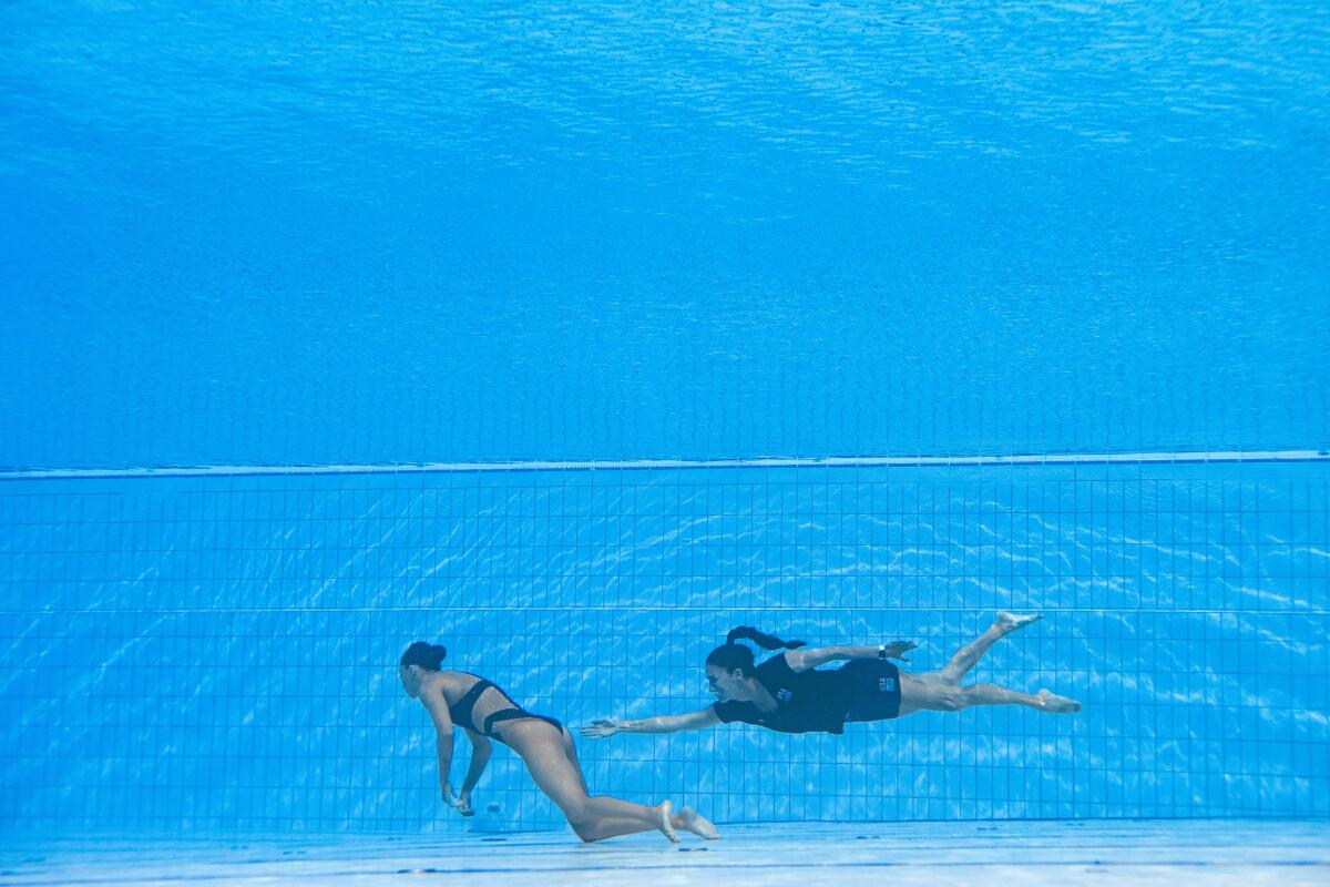 A woman swims toward a woman who is floating unconscious.