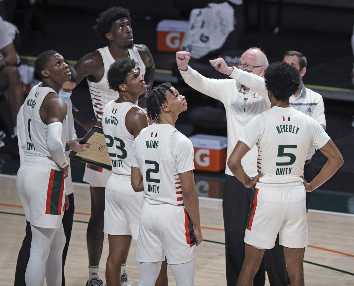 Miami coach Jim Larranaga talks with players as they look up toward the board showing the Hurricanes trailing Purdue during the first half of an NCAA college basketball game Tuesday, Dec. 8, 2020, in Coral Gables, Fla. (Al Diaz/Miami Herald via AP)
