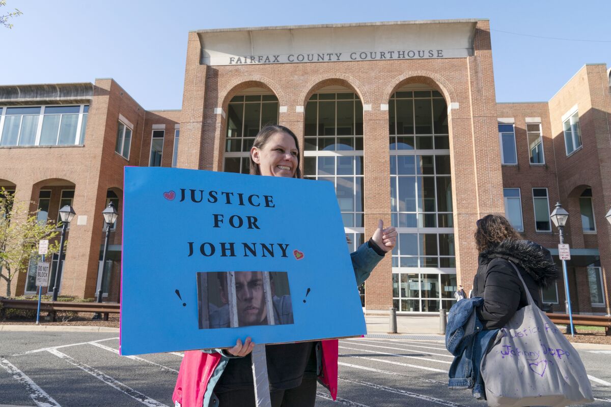 A woman holds a sign reading "Justice for Johnny" outside a courthouse.