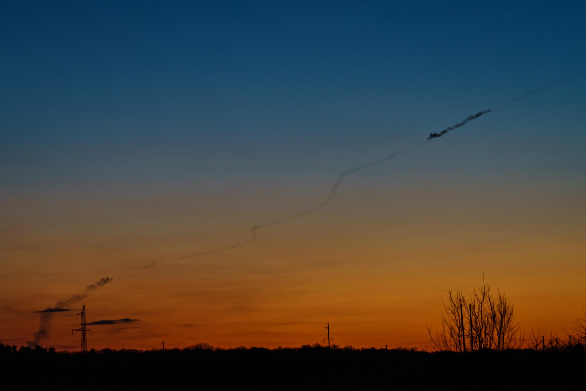 A smoke trail from a rocket launch in the evening sky colored orange, yellow and blue in Baryshivka, Ukraine.