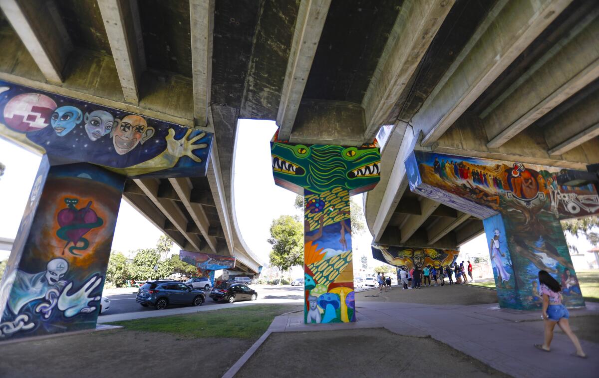 A woman walks among colorfully painted art work on Coronado bridge supports in Barrio Logan.