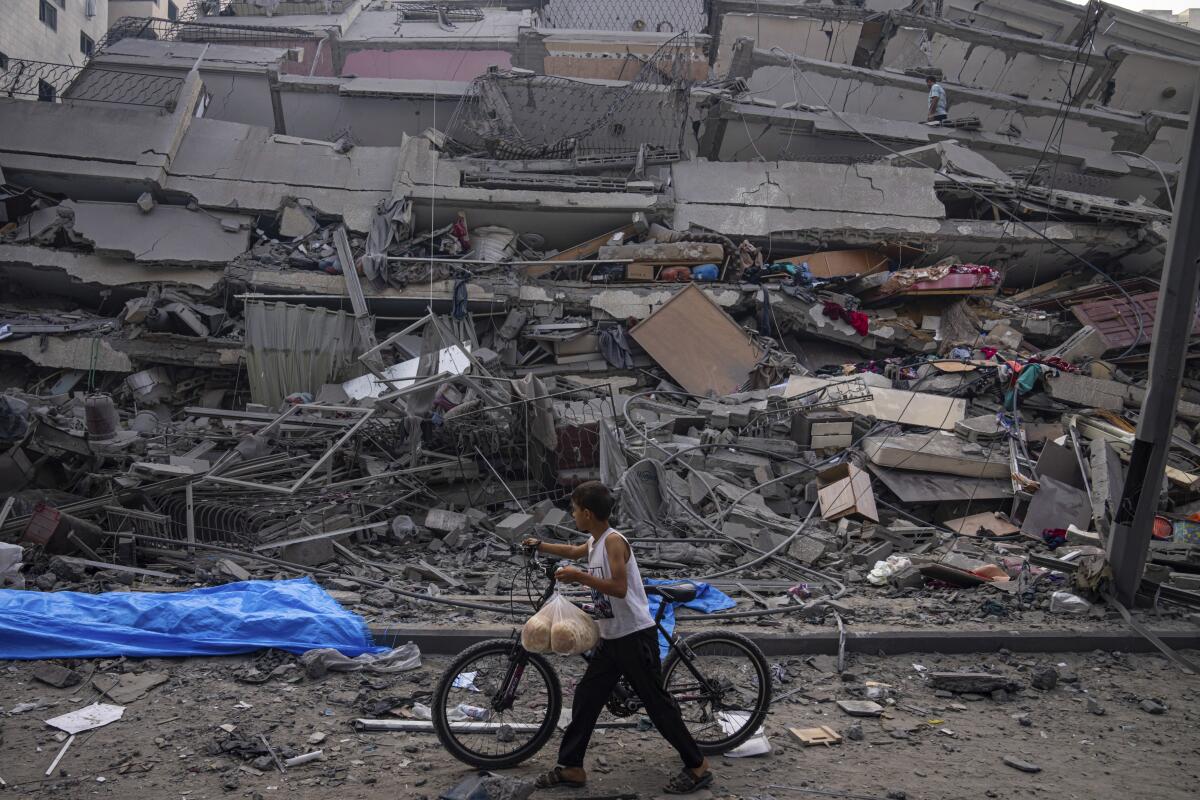 A child walking a bicycle past a building reduced to rubble