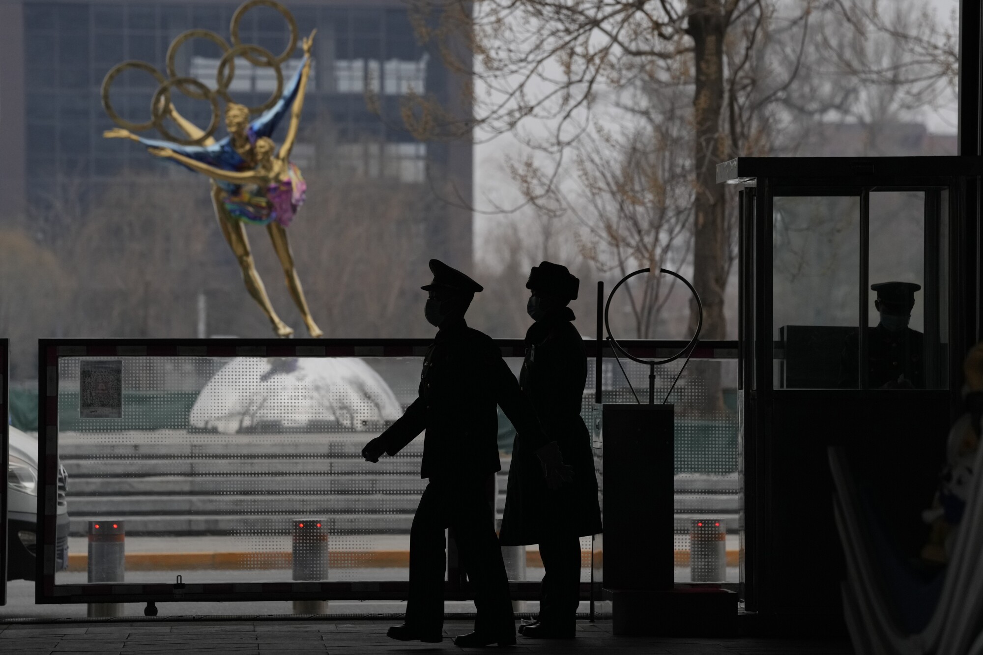 Two people stand in silhouette before a sculpture depicting two figure skaters with the Olympic rings