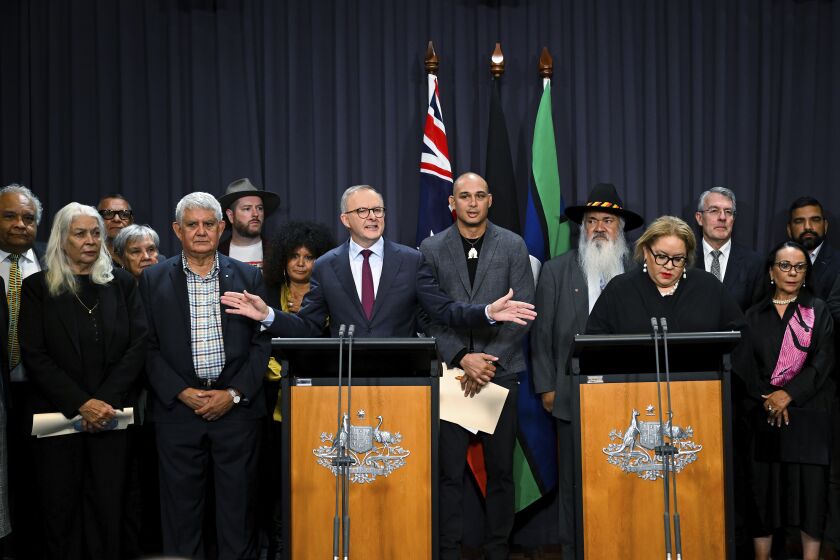 Australian Prime Minister Anthony Albanese, at the left podium, is surrounded by members of the First Nations Referendum Working Group as he speaks during a press conference at Parliament House in Canberra, Thursday, March 23, 2023. The Australian government released the wording of a referendum question that promises the nation's troubled Indigenous population a greater say on policies that effect their lives. (Lukas Coch/AAP Image via AP)