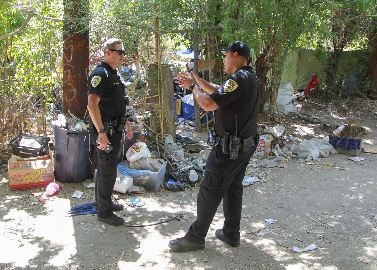 National City police department police officers Steven Anderson (left) and Dan Duran, who are part of the Homeless Outreach Team, reach out to residents of an area called The Jungle on August 30, 2019 in National City, California.