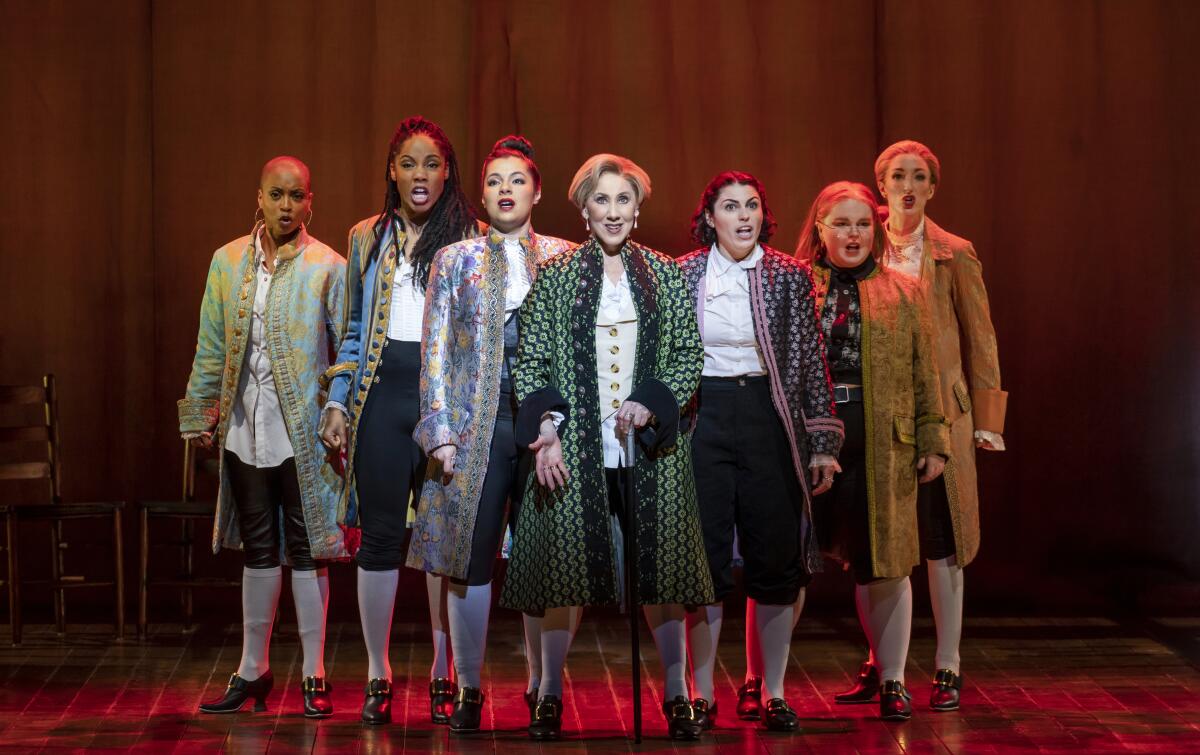 Seven women sing on stage dressed as the Founding Fathers.