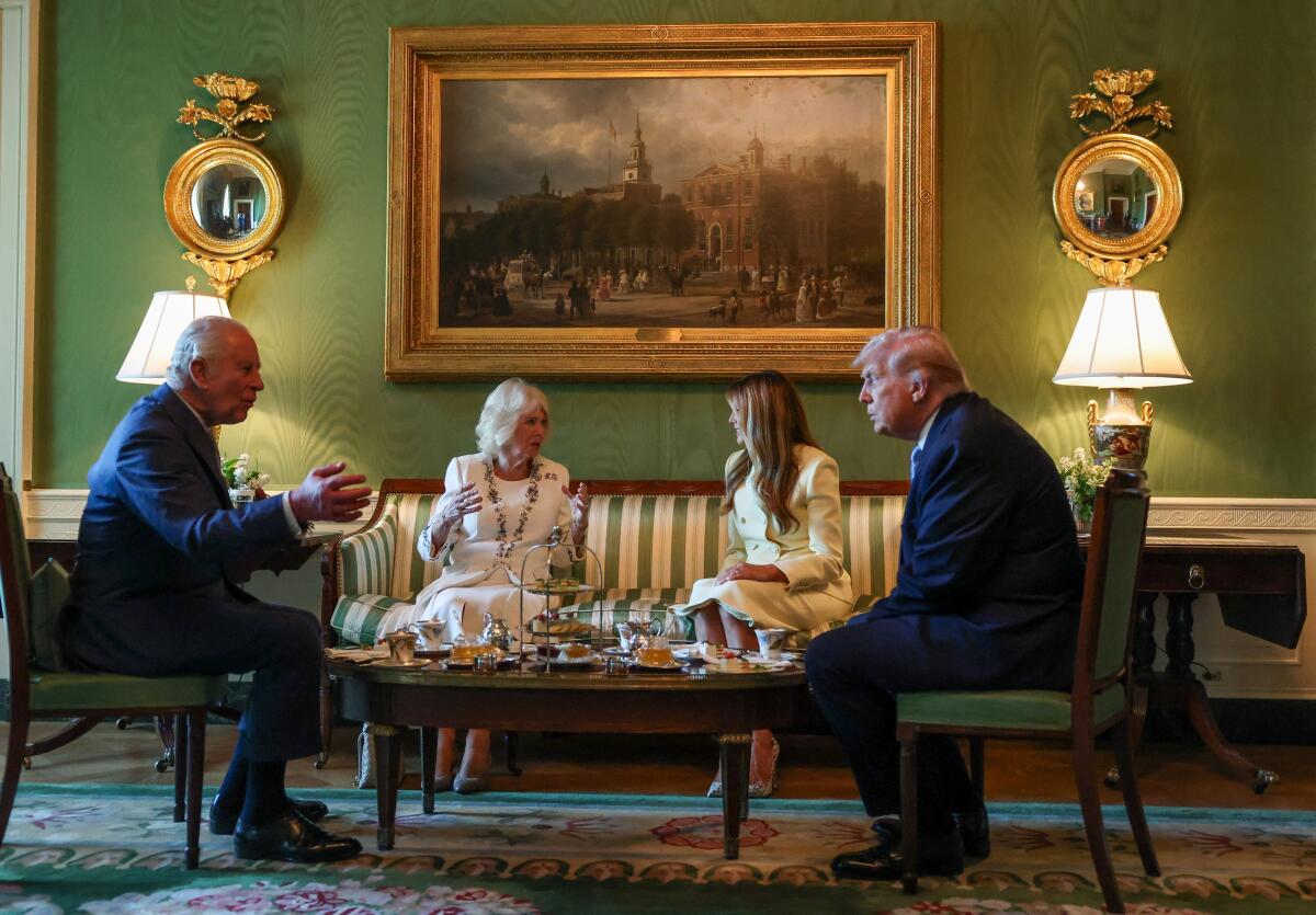 Four people seated around a table with food in a green room with a gold-framed painting