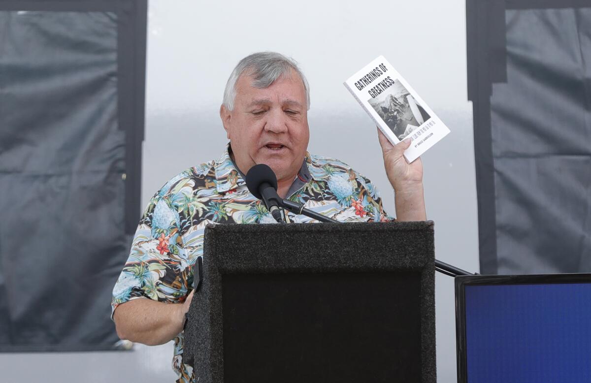 Local surf hero Bruce Gabrielson shows his book "Gatherings of Greatness" as he makes comments during Thursday's ceremony.
