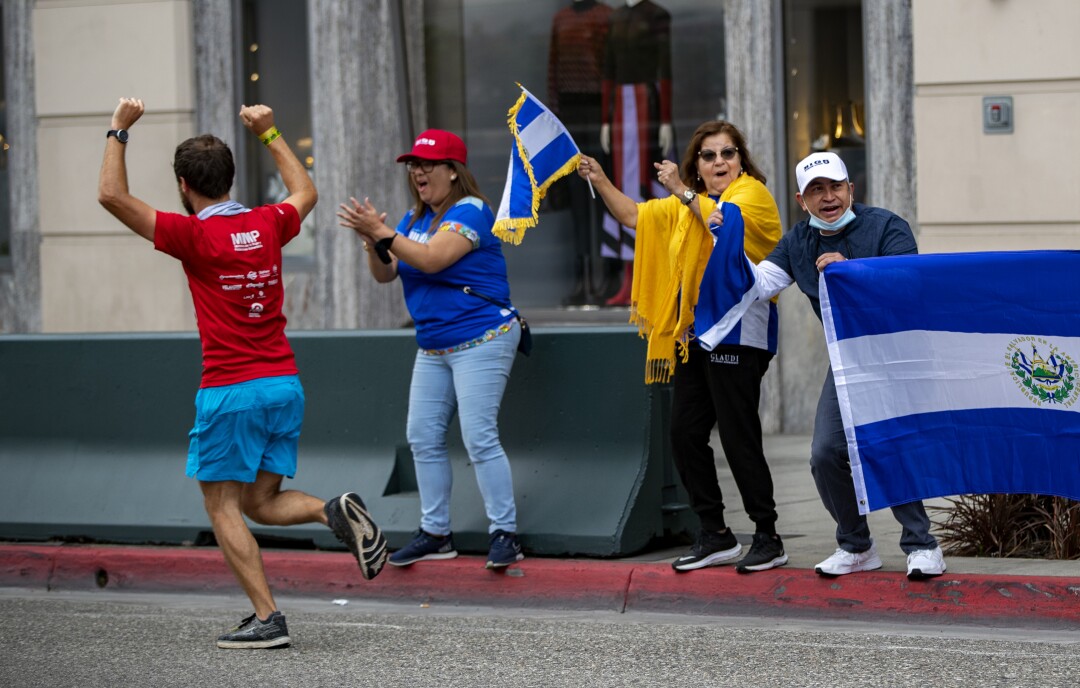 Fans hold flags and cheer as runners pass by on Rodeo Drive