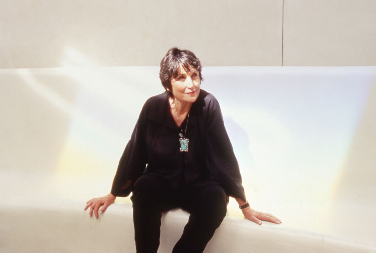 A woman with short hair and wearing all black is seen photographed against an all-white background.