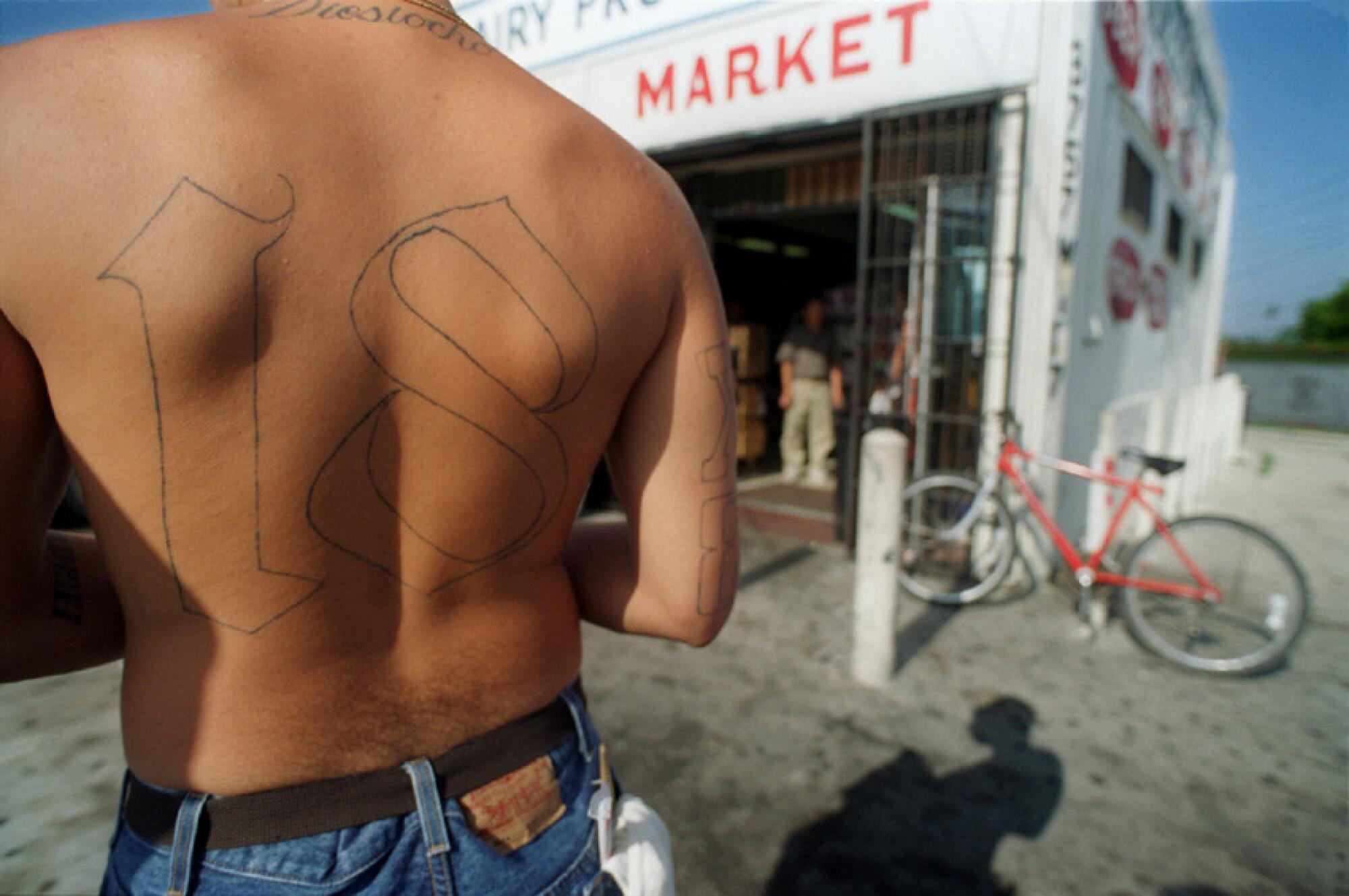 A tattooed "18" covers the back of a shirtless gang member.