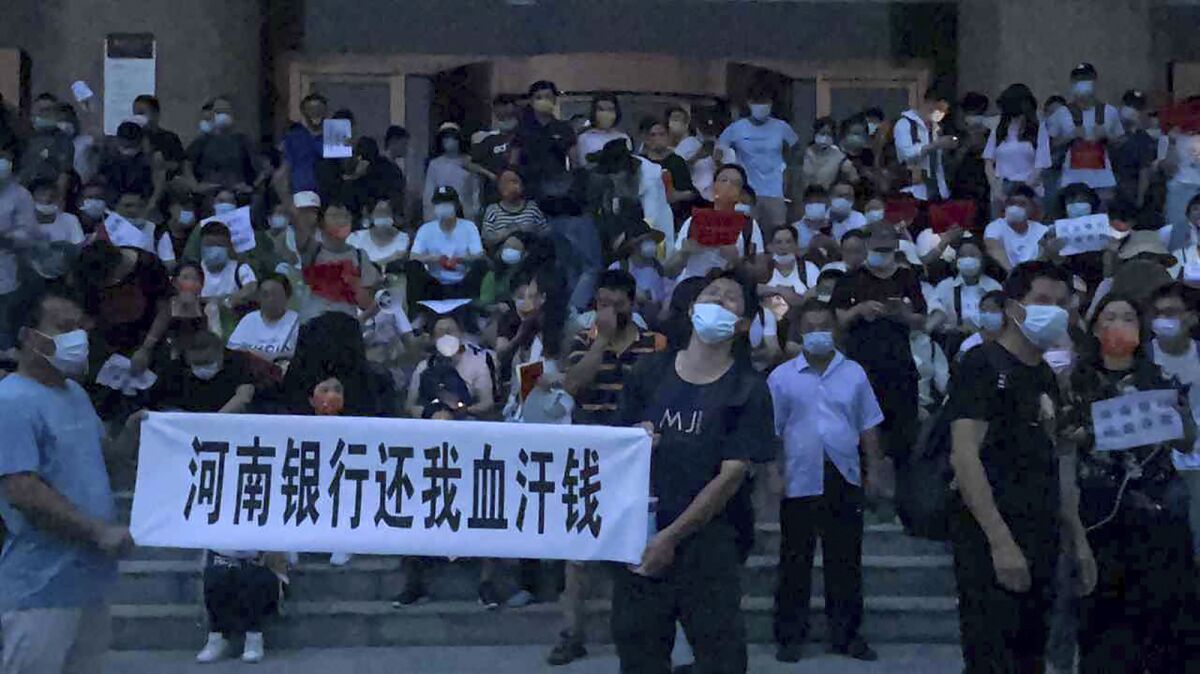 In this photo released by Yang on Sunday, July 10, 2022, people hold banners and chant slogans stage a protest at the entrance to a branch of China's central bank in Zhengzhou in central China's Henan Province. A large crowd of angry Chinese bank depositors faced off with police Sunday, some reportedly injured as they were roughly taken away, in a case that has drawn attention because of earlier attempts to use a COVID-19 tracking app to prevent them from mobilising. (AP Photo/Yang)
