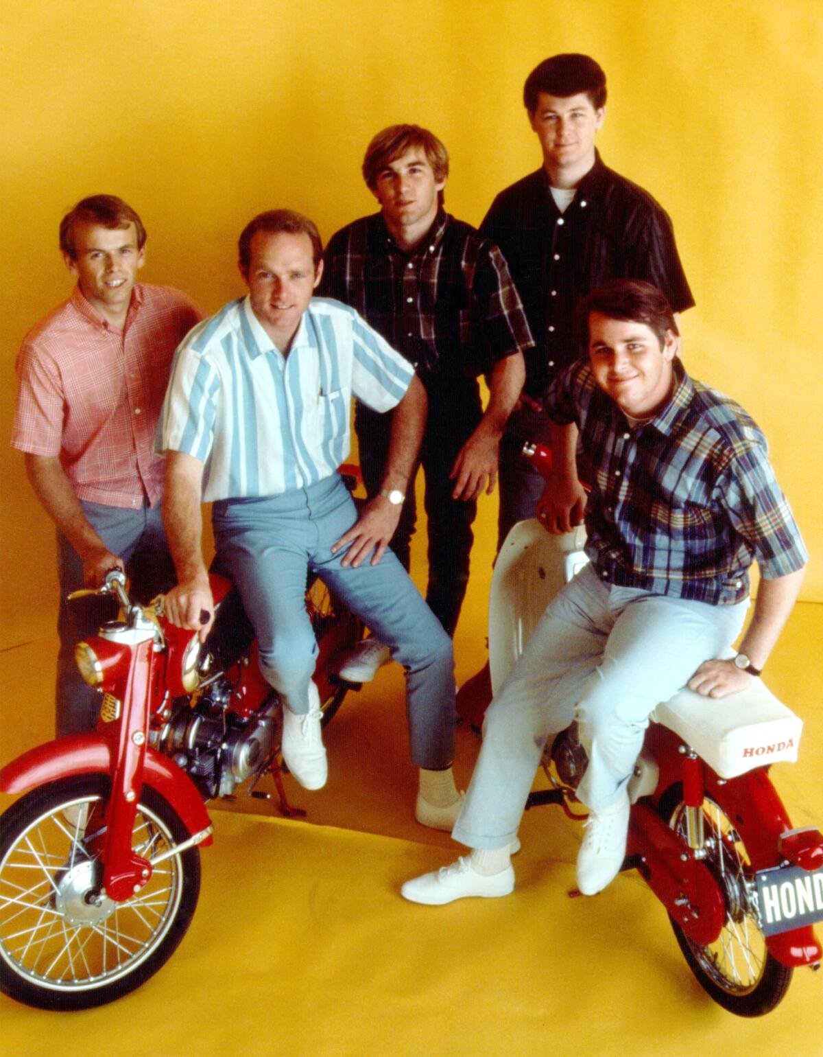 The Beach Boys sitting on and clustered around an old-fashioned red bike