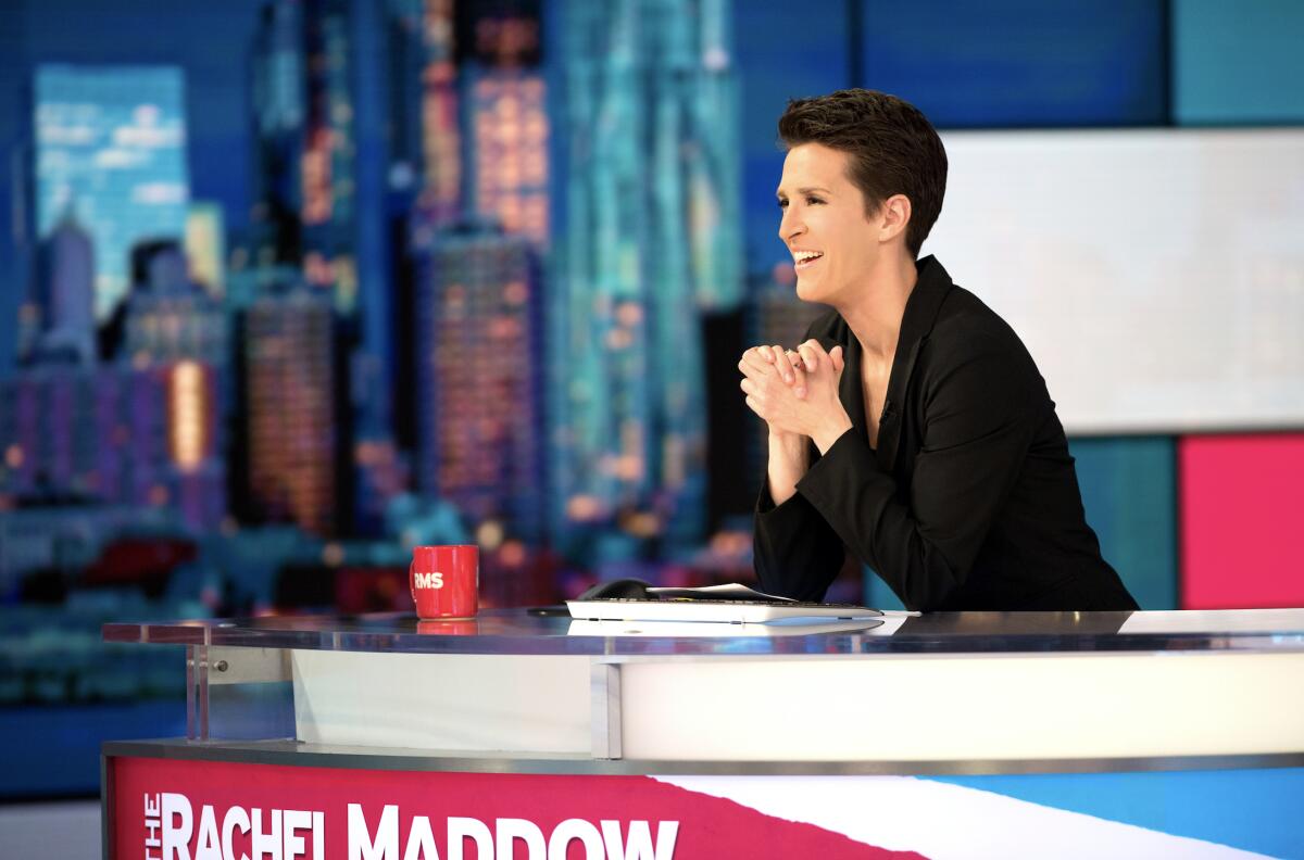 A woman sits at a desk on a TV news set.