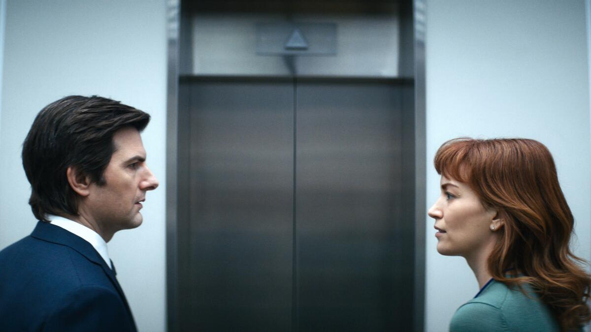 A man and a woman face each other, standing in front of closed elevator doors.