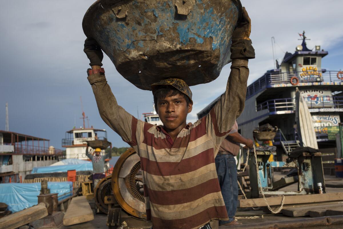 Michael Urquilla carries scrap metals for recycling to a cargo ship, at the Masusa port in Iquitos, Peru, Friday, March 19, 2021. It's been almost a year that dozens who died of COVID-19 were secretly buried in a field in Iquitos, a city in Loreto state in the heart of the Peruvian Amazon. Nobody is able to explain why the clandestine burials were held. (AP Photo/Rodrigo Abd)