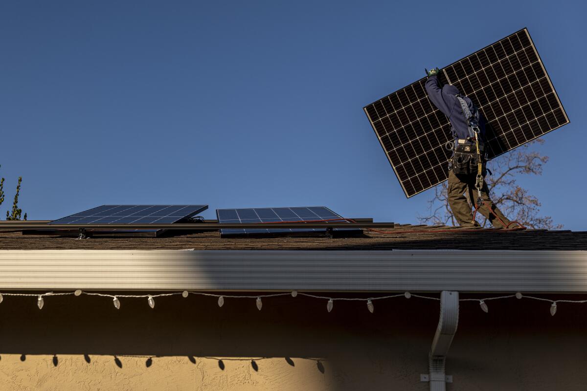 A contractor carries a solar panel on the roof of a home in San Jose.