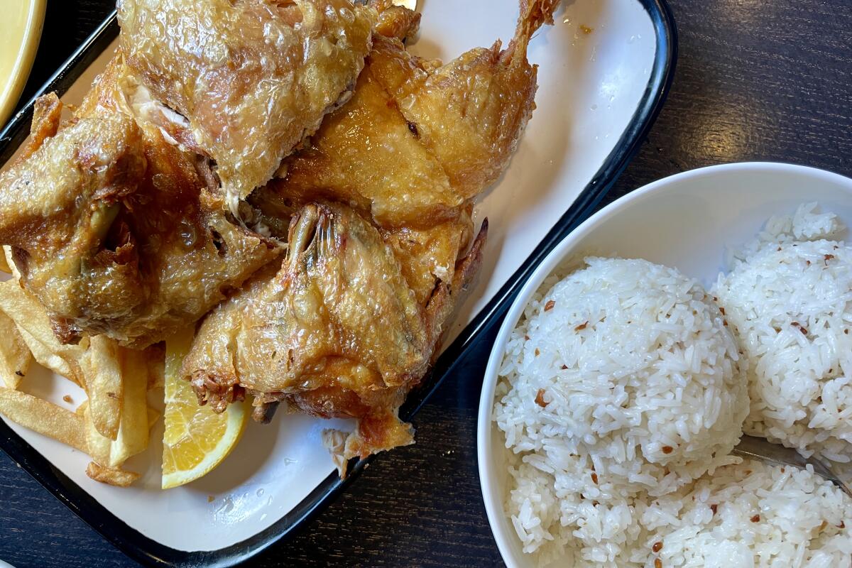A plate of fried chicken next to a bowl of scoops of garlic rice.
