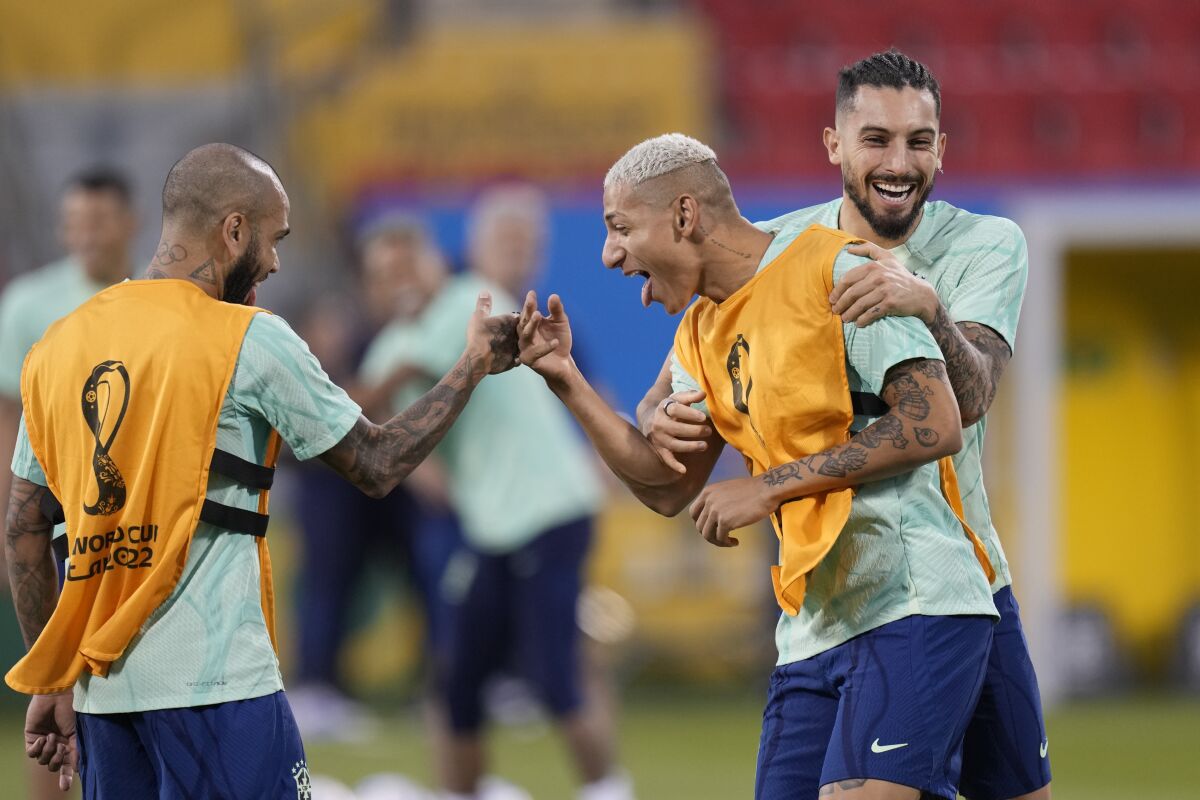 Brazil's Richarlison, center, jokes with teammates Alex Telles, right, and Dani Alves during a training session at the Grand Hamad stadium in Doha, Qatar, Sunday, Nov. 27, 2022. Brazil will face Switzerland in a group G World Cup soccer match on Nov. 28. (AP Photo/Andre Penner)