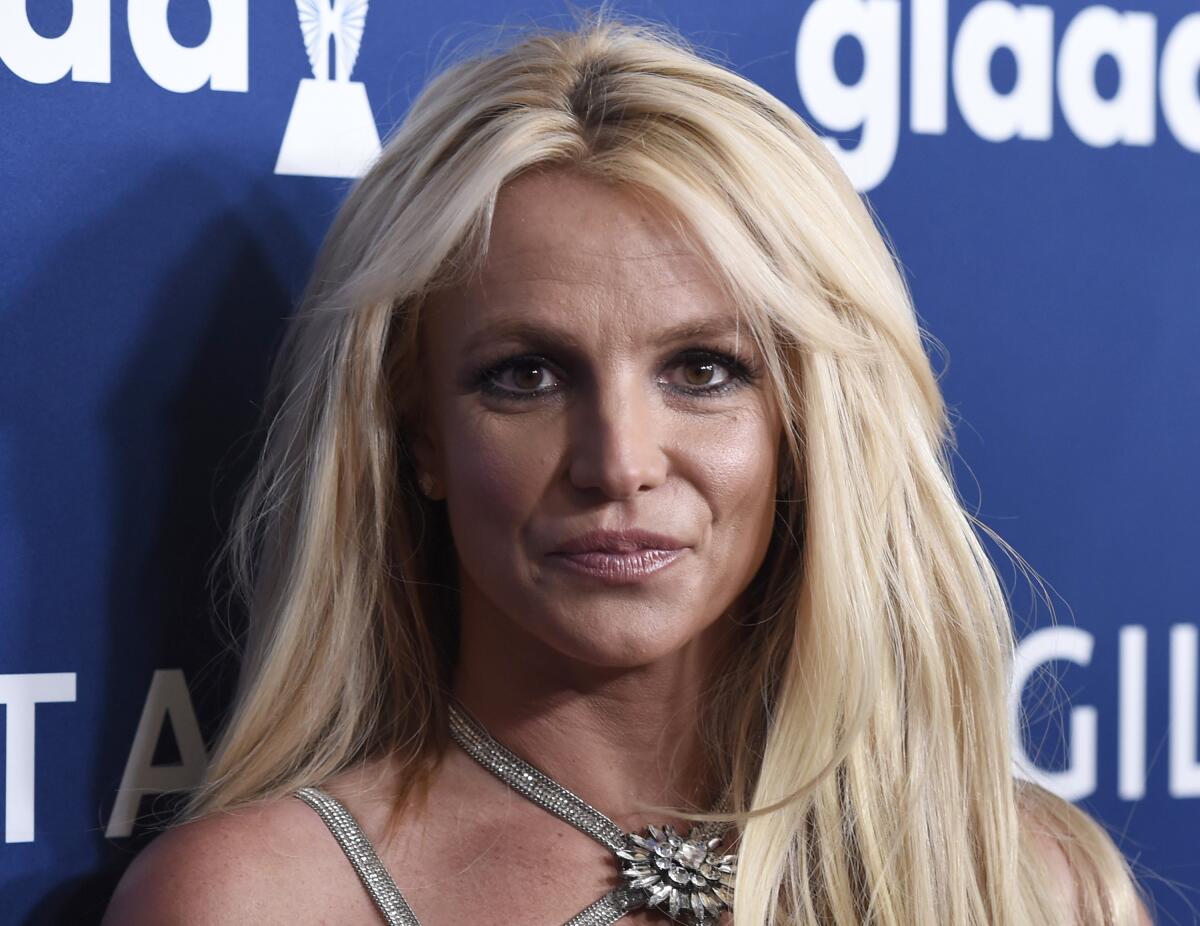 Britney Spears posing with a serious face against a blue background with her blond hair down