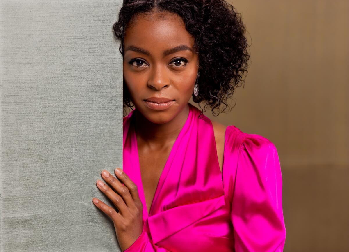 Danielle Deadwyler in a vibrant pink dress leans against a wall for a portrait.