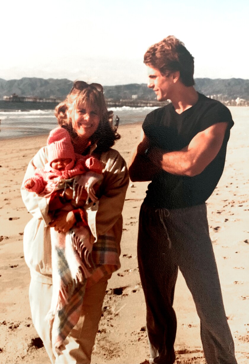 Debra Bilton holds Chrysta in her arms on a beach in Los Angeles, California while father Jeffrey Harrison looks on, 1984.