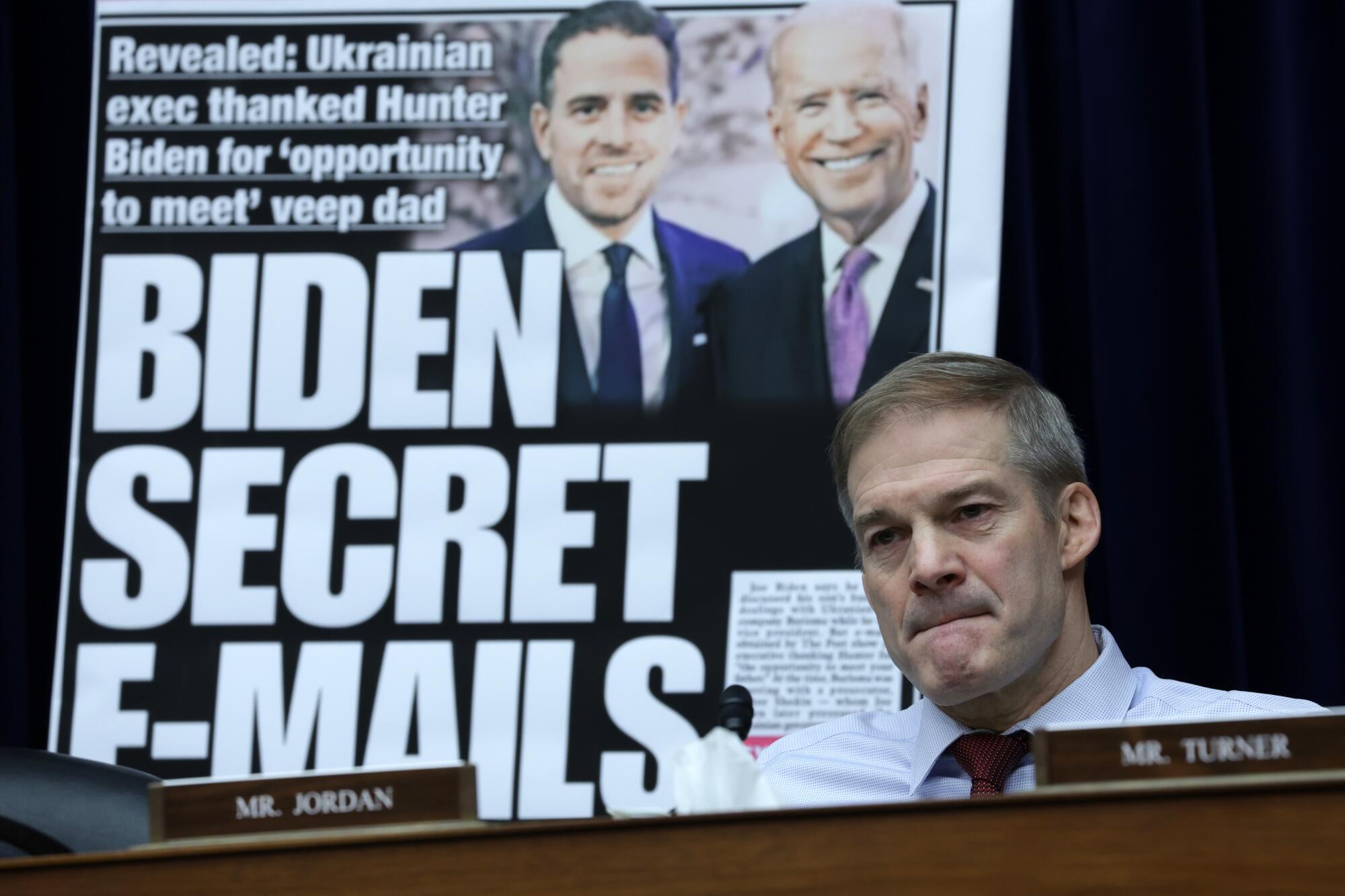 Jim Jordan seated on dais before an image of a tabloid showing President and Hunter Biden