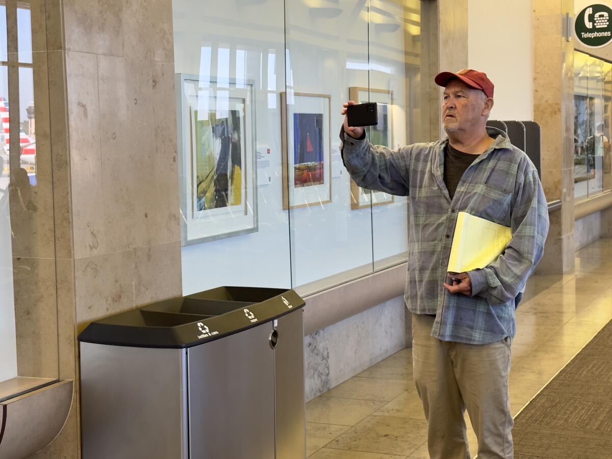 A visitor takes a picture of artwork in the Festival of Arts exhibit at John Wayne Airport.