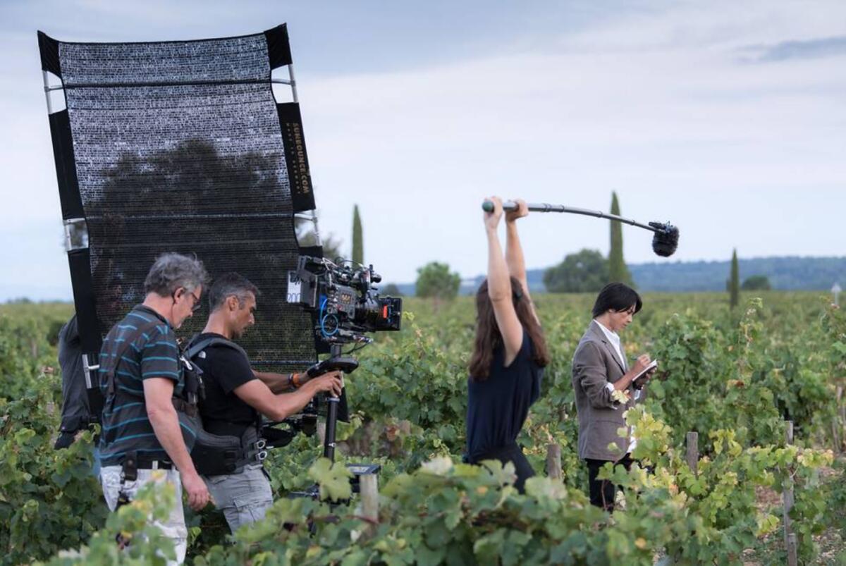 Filming a scene in "Drops of God," actor Tomohisa Yamashita stands among vines in France, taking notes. Crew members watch.