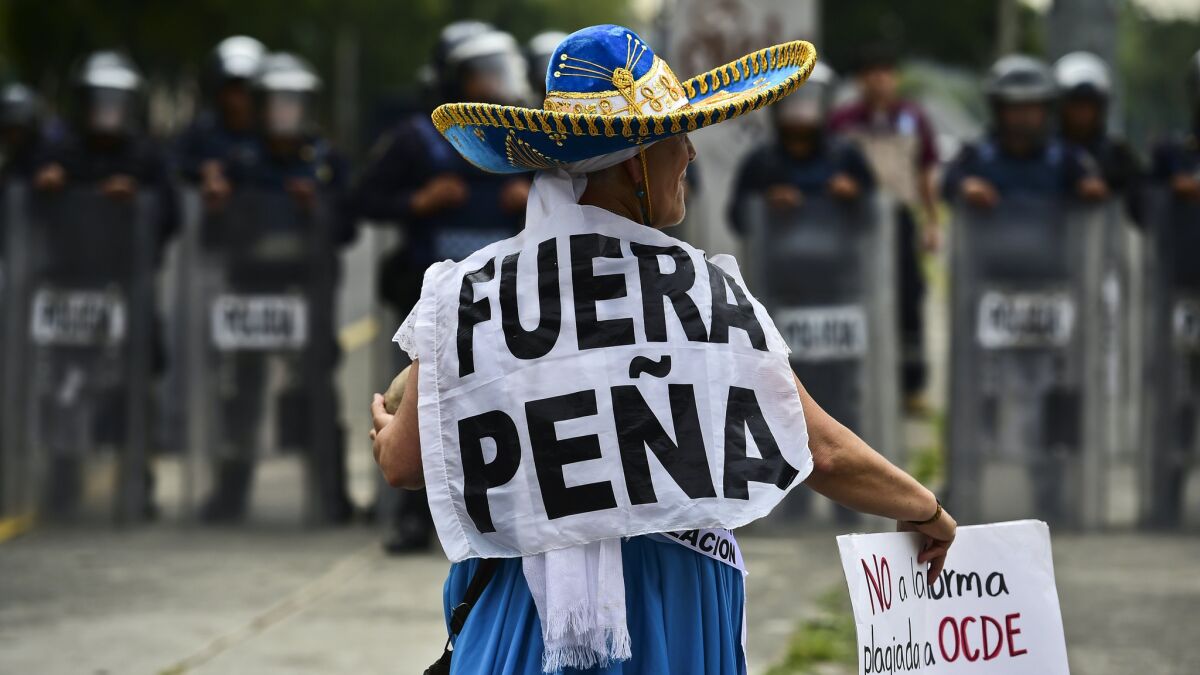 A teacher protesting a government education reform plan wears a sign saying "Out with Peña," a reference to the Mexican president.