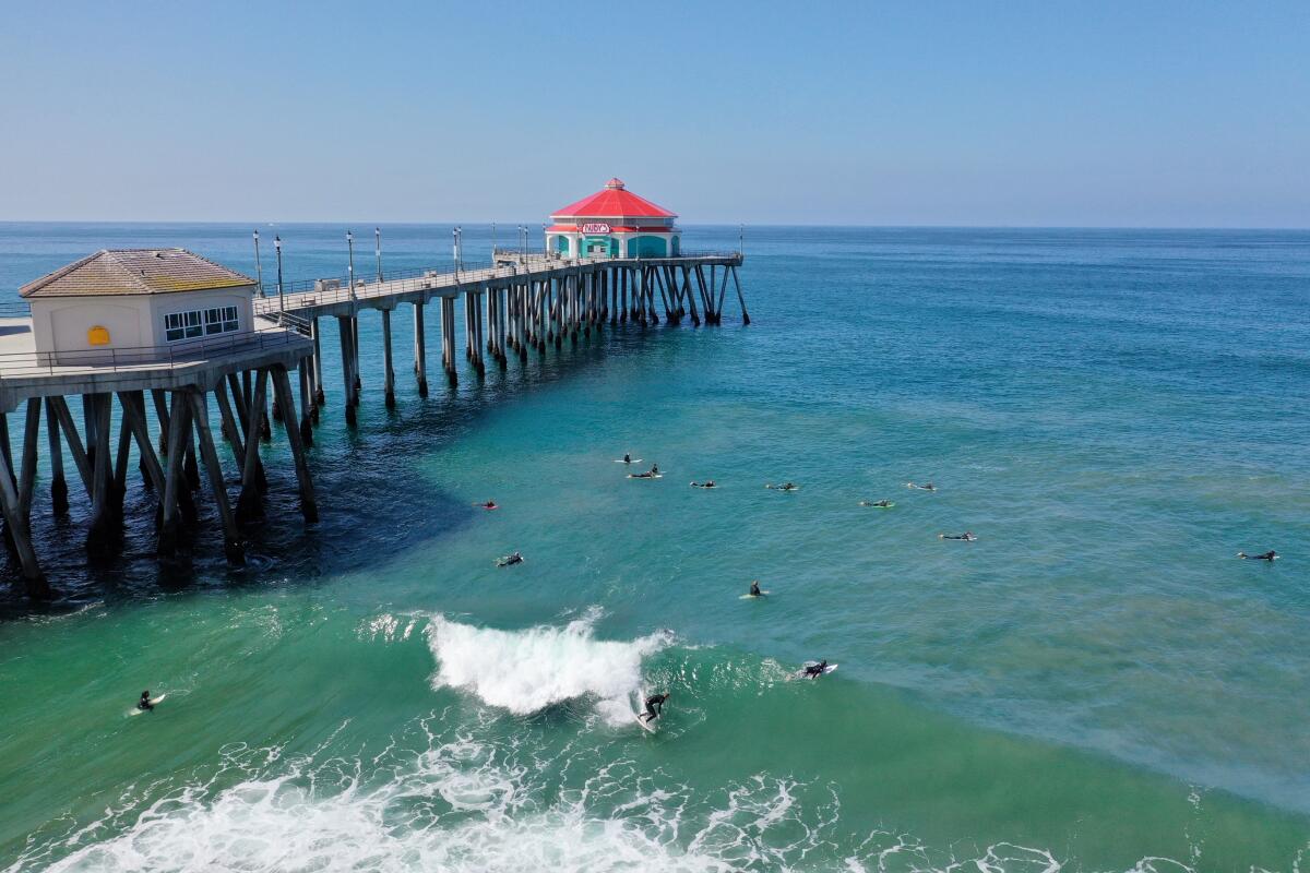 Surfers off the Huntington Beach Pier on Friday ignore the governor's order to close Orange County beaches.