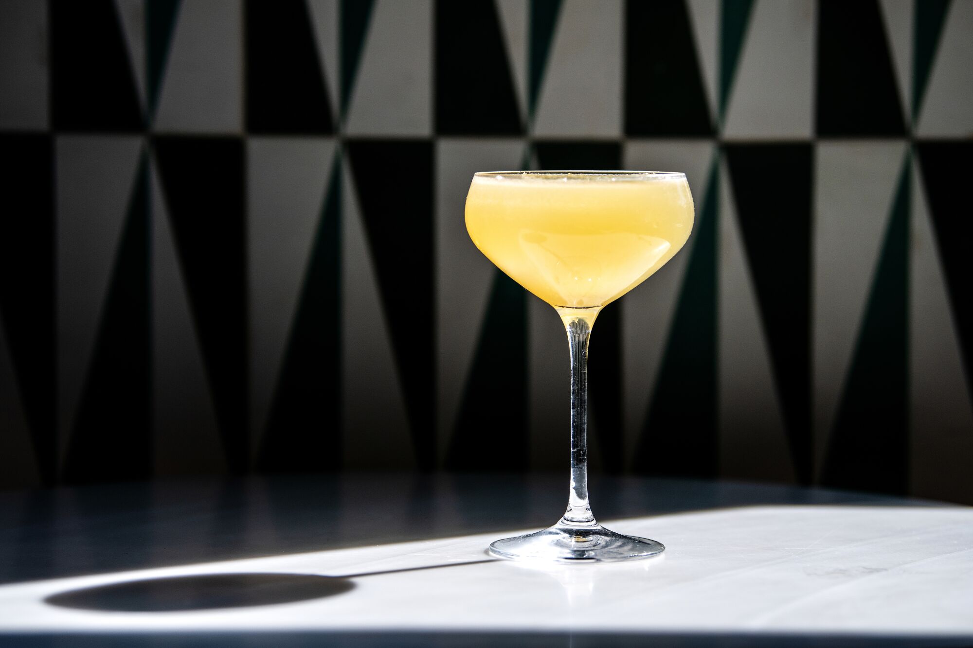 A yellow cocktail in a coupe glass on a sleek counter.