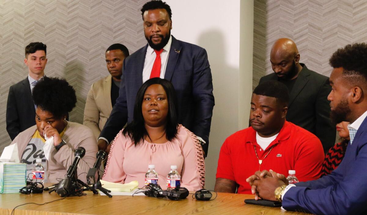 Amber Carr, left, wipes a tear as her sister Ashley Carr, center, talks about their sister, Atatiana Jefferson, as their brother, Adarius Carr, right and attorney Lee Merritt, standing, listen during a news conference Monday, Oct. 14, 2019 in downtown Dallas. The family of the 28-year-old black woman who was shot and killed by a white police officer in her Fort Worth home as she played video games with her 8-year-old nephew expressed outrage that the officer has not been arrested or fired. (Irwin Thompson/The Dallas Morning News via AP)