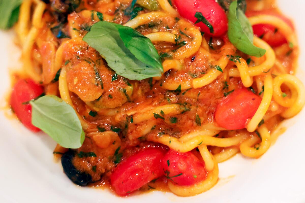 Close up of Puttanesca spaghetti, with a red sauce, fresh basil and tomato.