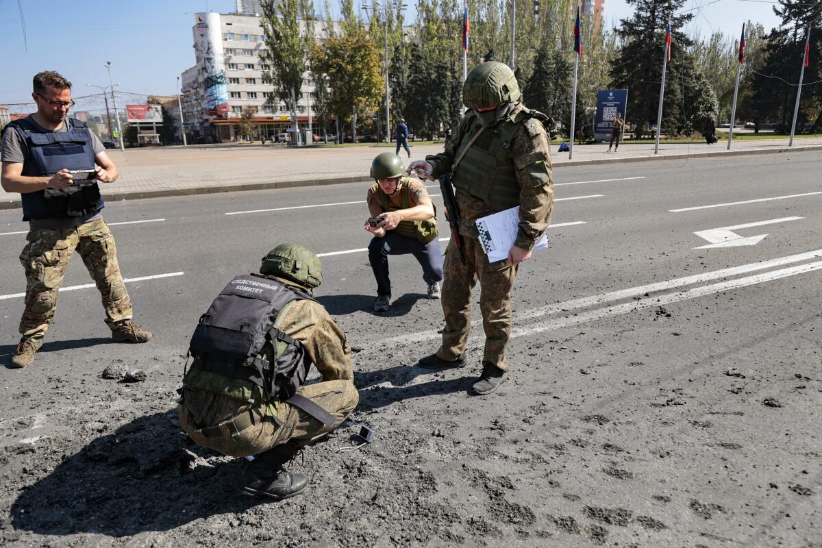 Four men in camouflage and bulletproof vests look carefully at a pockmarked street