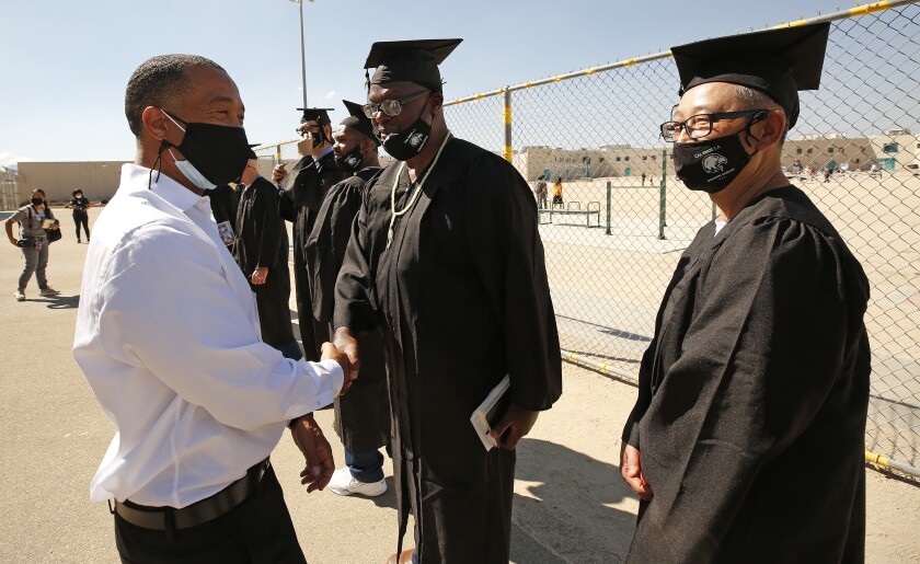 A man shakes hands with a graduate in cap and gown.