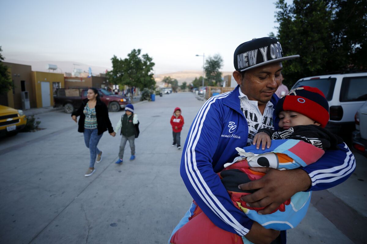 A man carries his youngest son as the family leaves their home in Tijuana for an asylum hearing in San Diego.