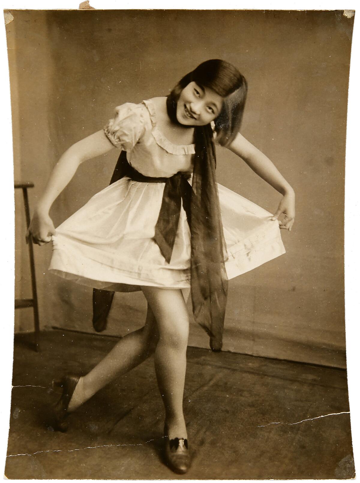 A sepia photograph of a young woman in a dress, curtsying