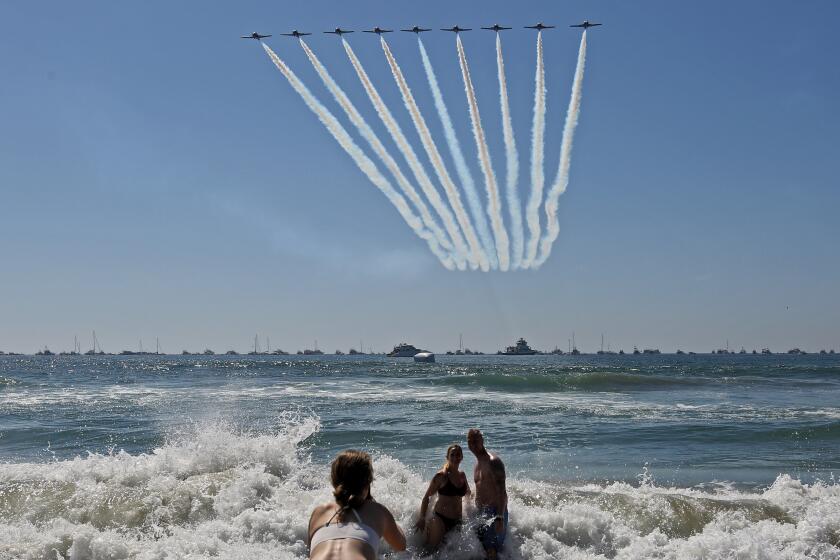 A coupe has their photo taken as the Canadian Forces Snowbirds pass by with a trail of smoke at the Great Pacific Airshow, in Huntington Beach, on Saturday, Oct. 5, 2019.