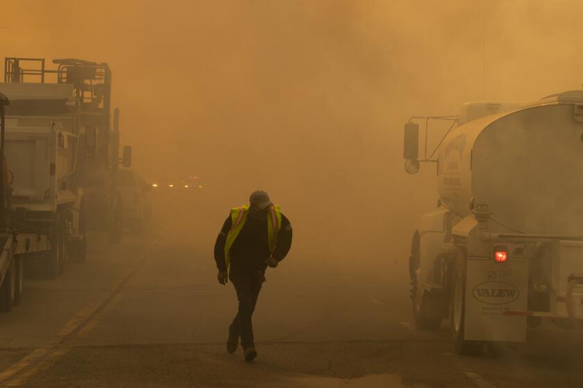A water truck operator runs through the thick smoke of the advancing Silverado Fire fueled by Santa Ana winds at the 241.