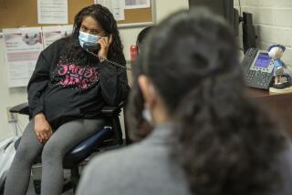 A woman wearing a medical mask holds a phone receiver in an office. 