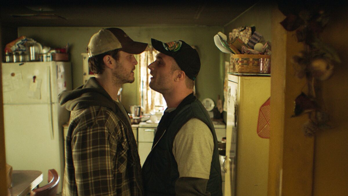 Two men in trucker caps go face to face in a kitchen in the movie “The Evening Hour.”