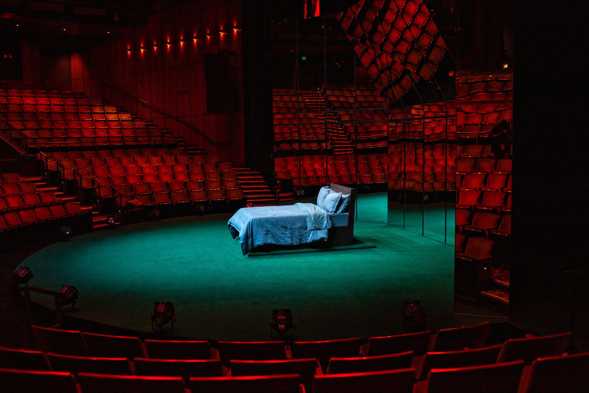 Red stage lighting blankets the seats in the Mark Taper Forum surrounding one of the beds on the set of "Slave Play."