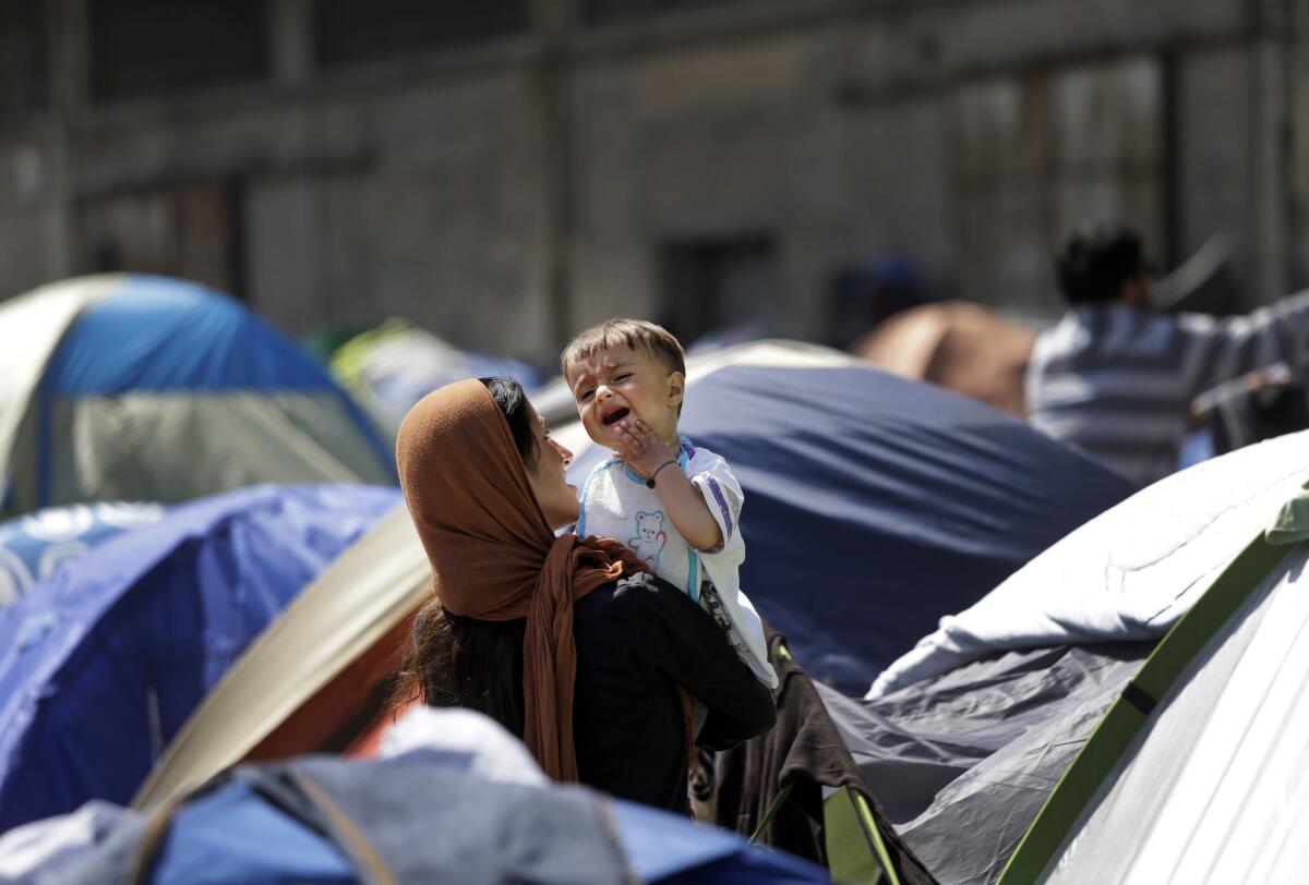 A woman holds a child among tents where migrants stay at the port of Piraeus. (Lefteris Pitarakis / Associated Press)