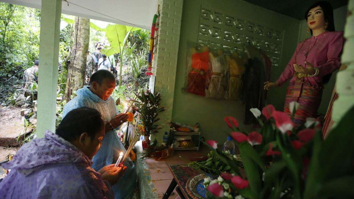 At one shrine, relatives of the missing boys and their coach kneel, light candles and incense and pray in front of a statue of a young woman wearing a pink traditional outfit, surrounded by flowers and other offerings.