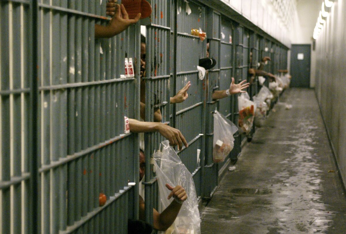 Inmates' arms and hands are seen through barred doors on a cell block at Men's Central Jail 